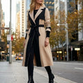 Colorblock Belted Longline Trench Coat worn by a female model, featuring contrasting panels, notch lapels, a waist belt, buckle cuff straps, and a longline silhouette.