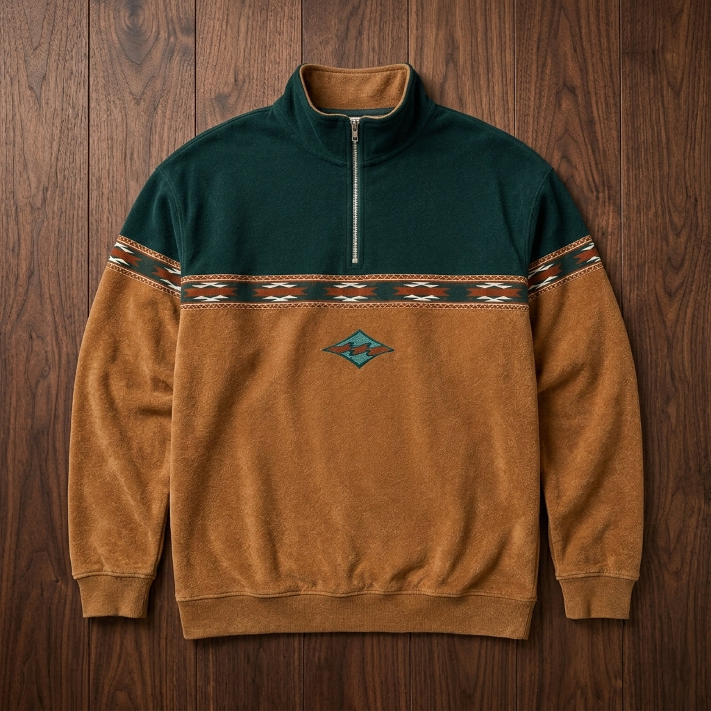 Teal and mustard colorblock quarter-zip pullover shown on a hanger, featuring a geometric chest band and embroidered motif.