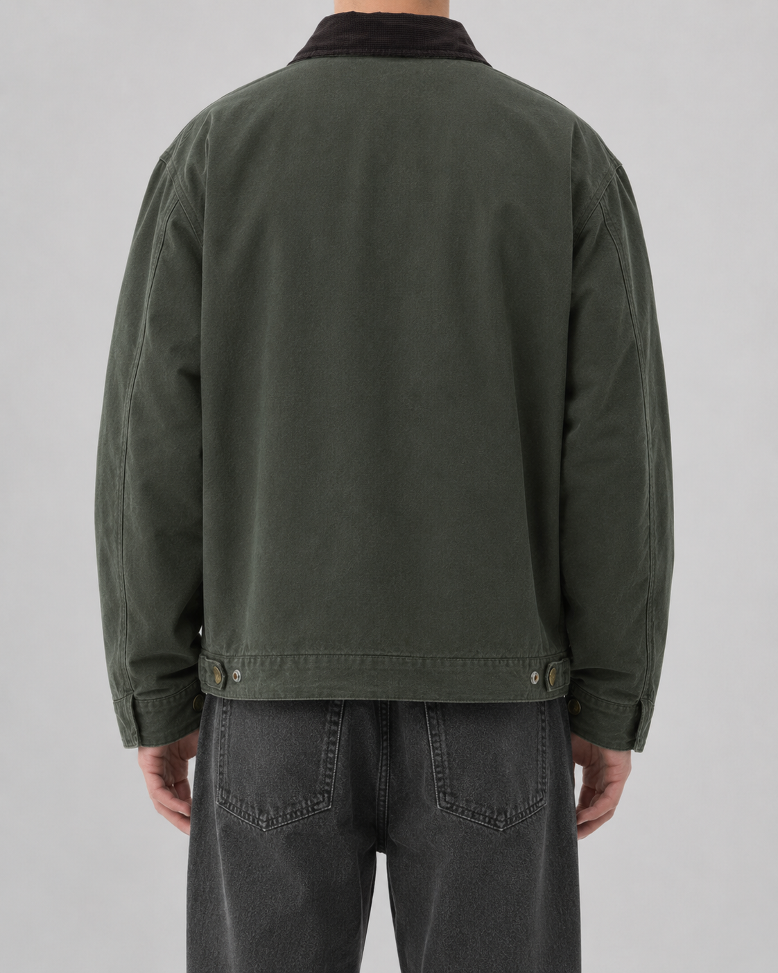 Back view of a model wearing the dark washed-green cotton canvas barn jacket paired with dark jeans.