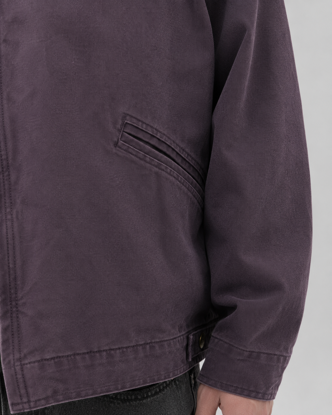 Close-up view of the stitched welt hand pocket and cuff detail on the muted purple cotton canvas jacket.