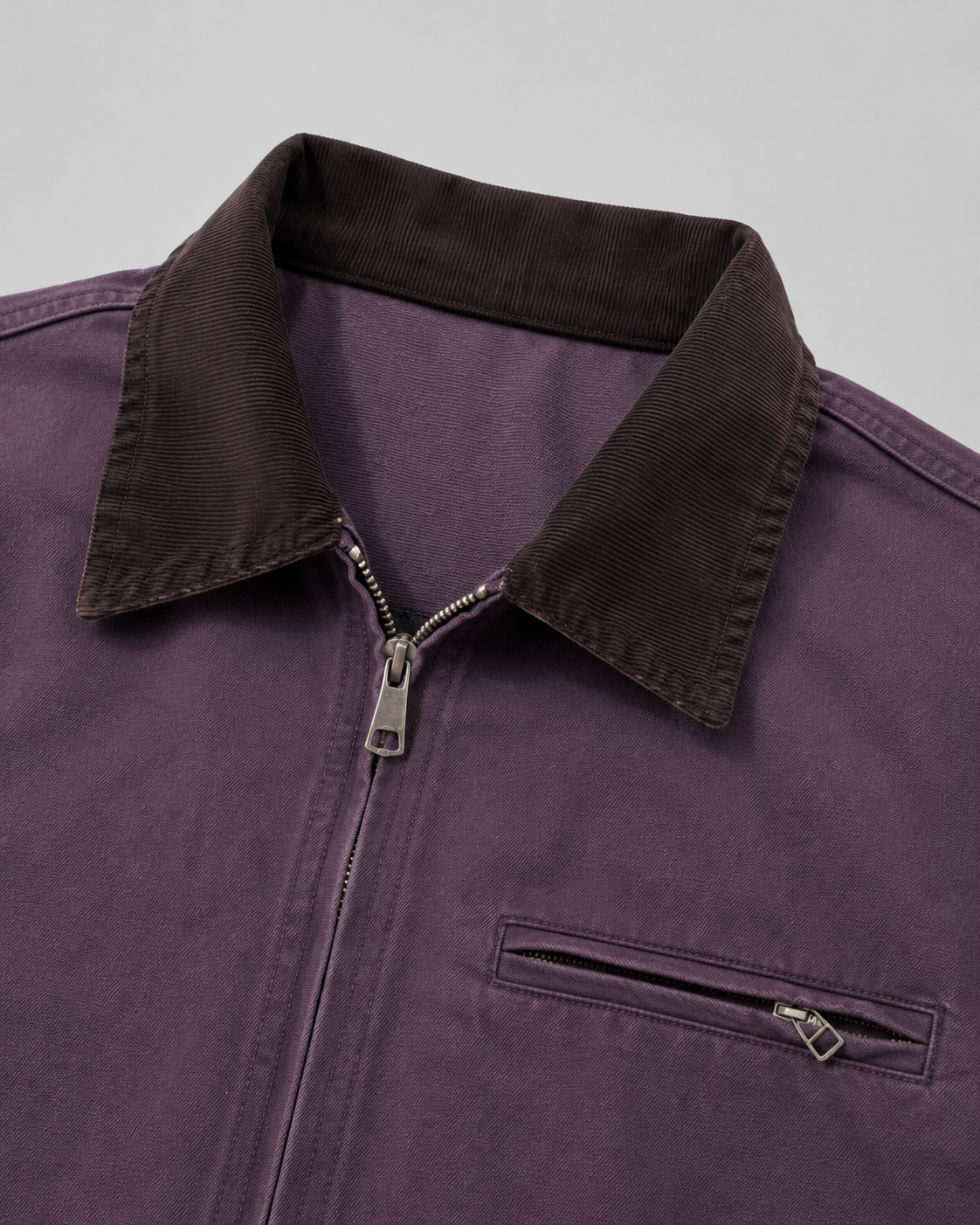 Close-up view of the dark brown corduroy collar, metal zipper pull, and chest zipper pocket on the muted purple barn jacket.