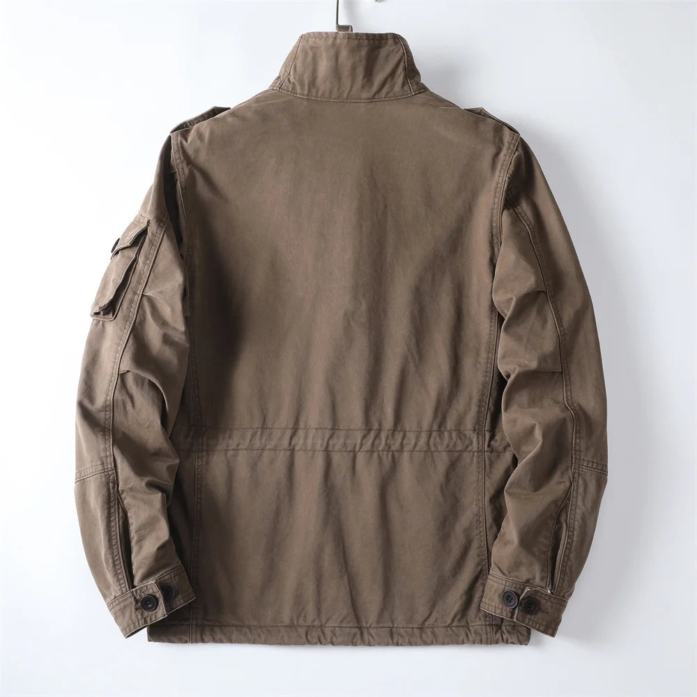 Back view of the brown cotton utility cargo jacket on a hanger showing the stand collar, shoulder yoke construction, clean back panel, and cuff button tabs.