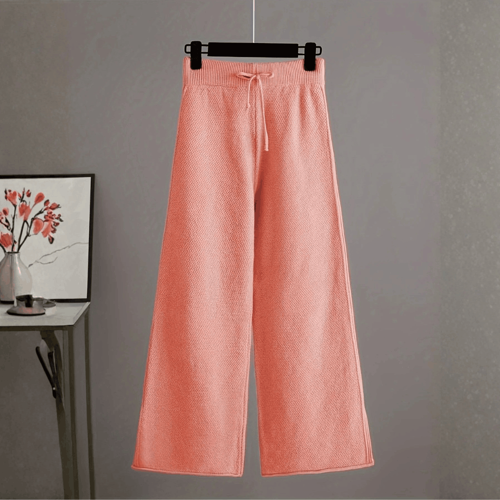 Front view of the high-waisted dusty pink wide-leg knit trousers on a hanger displaying the drawstring waistband.