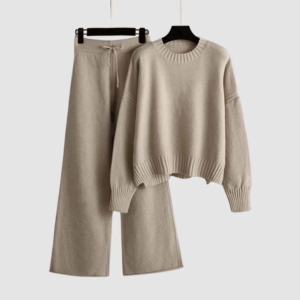 Full layout of an oat beige knit lounge set displayed on hangers, featuring a relaxed crewneck sweater with ribbed trim and matching high-waisted wide-leg pants with a drawstring waistband.