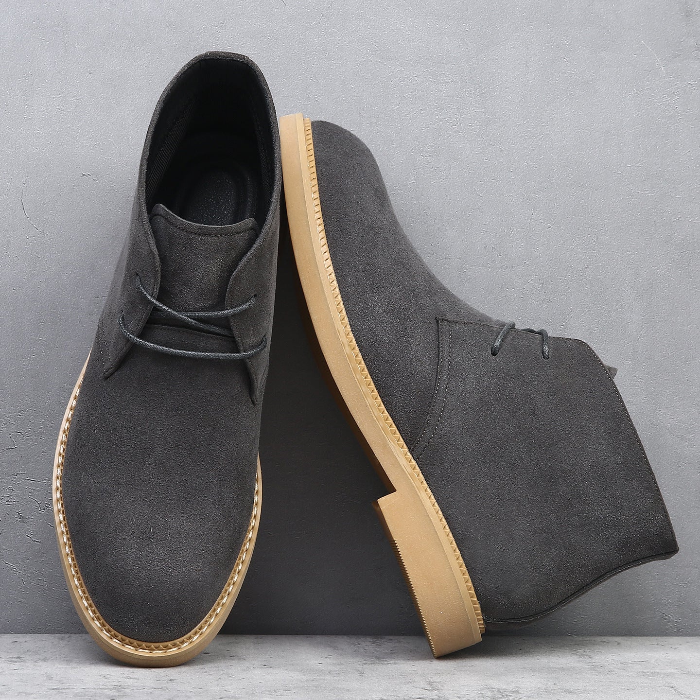 Charcoal suede desert boots with a plain toe, lace-up closure, and a flat, tan wedge sole featuring visible welt stitching.