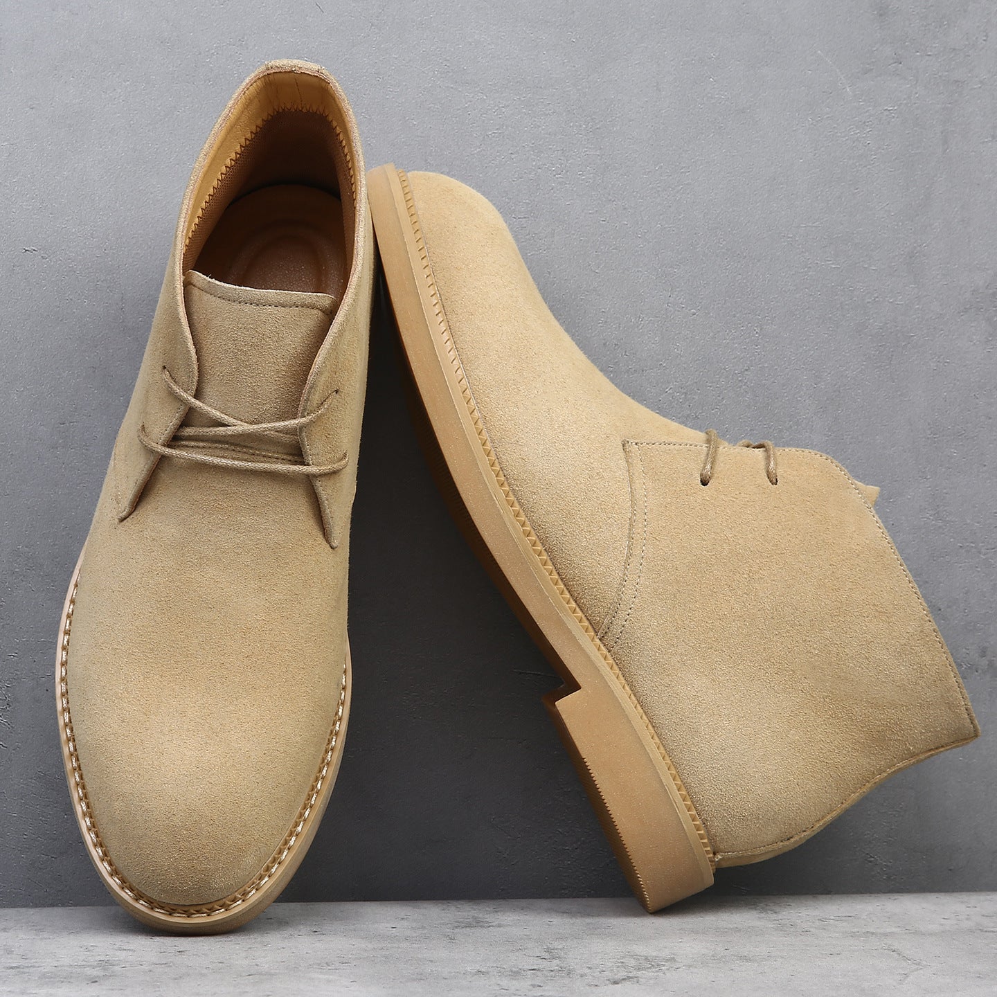 Tan suede desert boots with a plain toe, lace-up closure, and flat wedge sole featuring visible welt stitching.