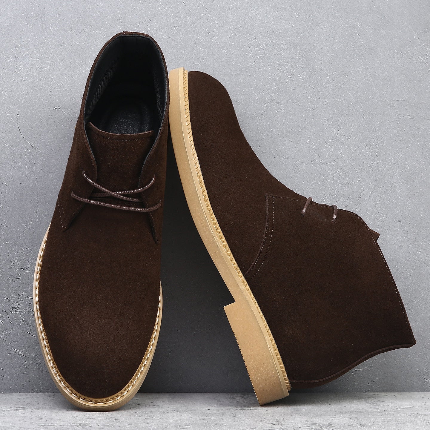 Dark brown suede desert boots with a plain toe, lace-up closure, and a flat, light-colored wedge sole with welt stitching.