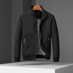 Black weather-resistant bomber jacket with a stand collar, zippered pockets, and a contrasting gingham-check lining.