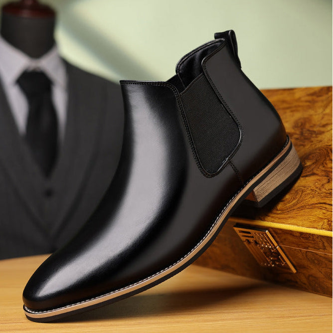 Black leather Chelsea boot with a pointed toe, elastic side panels, stitched welt, and a low stacked wooden heel.