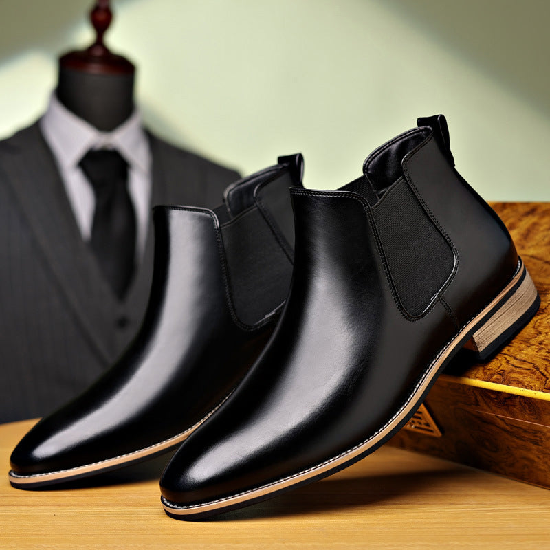 Black leather Chelsea boots with pointed toes, elastic side panels, and a low stacked heel on a wooden surface.