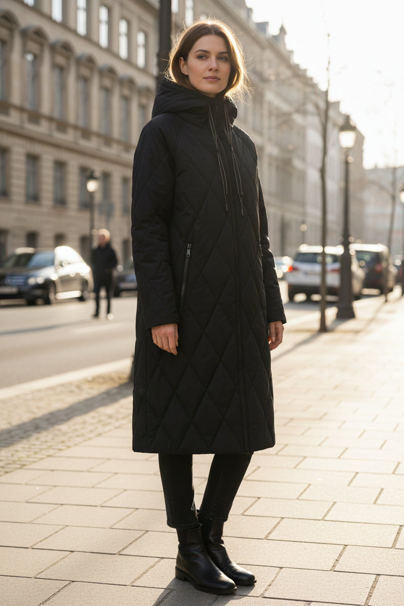 Black Diamond-Quilted Longline Coat worn by a female model outdoors, featuring a drawstring hood, diamond-quilted design, two-way zip front, and longline fit.