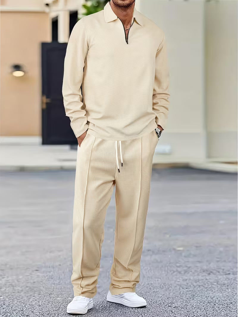 Man wearing a cream quarter-zip sweatshirt with matching drawstring jogger pants and white sneakers.