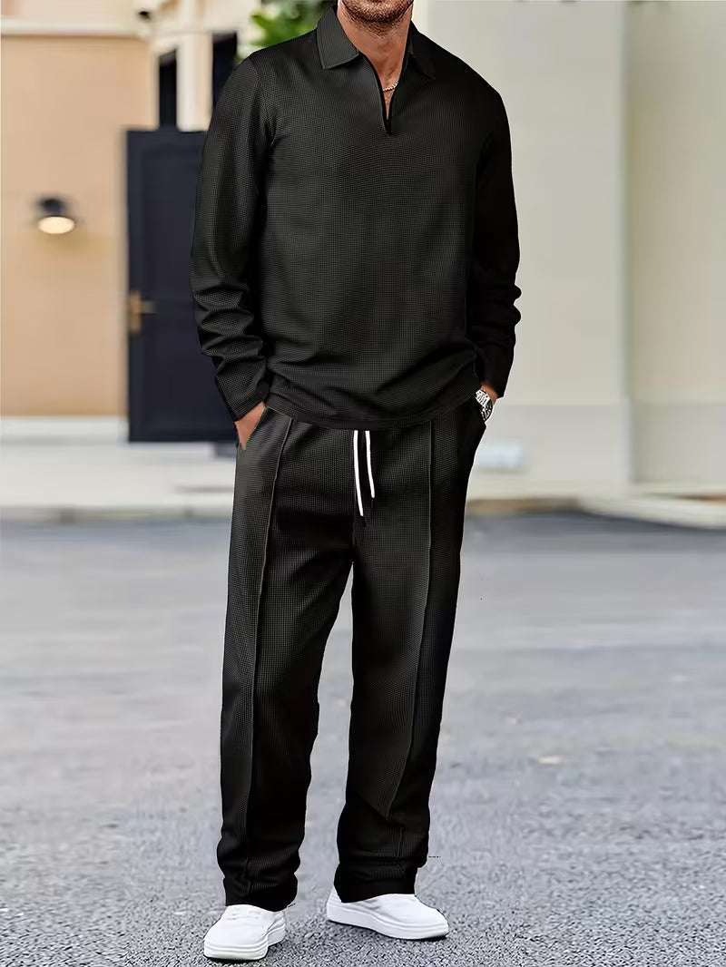 Man wearing a black quarter-zip sweatshirt with matching drawstring jogger pants and white sneakers in a relaxed casual outfit.