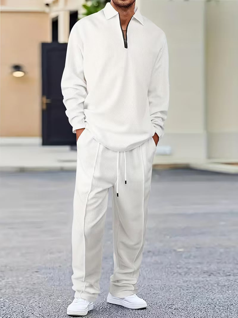 Man wearing a white quarter-zip sweatshirt with matching drawstring jogger pants and white sneakers in a casual outdoor setting.