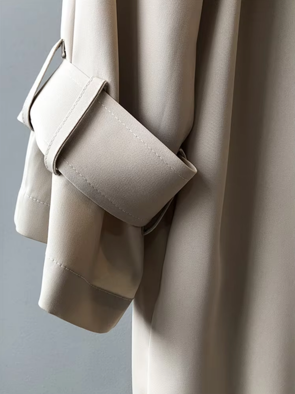 Close-up of the trench coat sleeve showing the button-tab cuff detail and tailored sleeve construction.