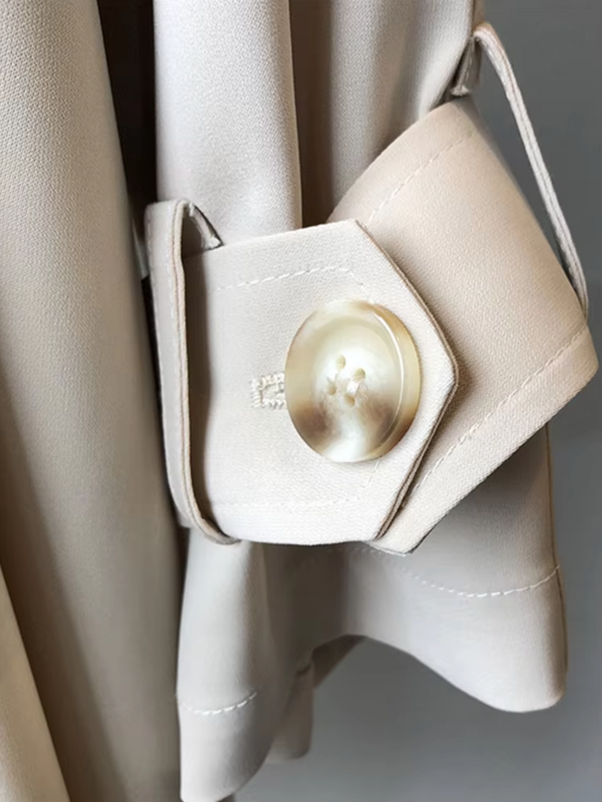 Close-up of the trench coat cuff highlighting the button-tab fastening and sleeve detail.