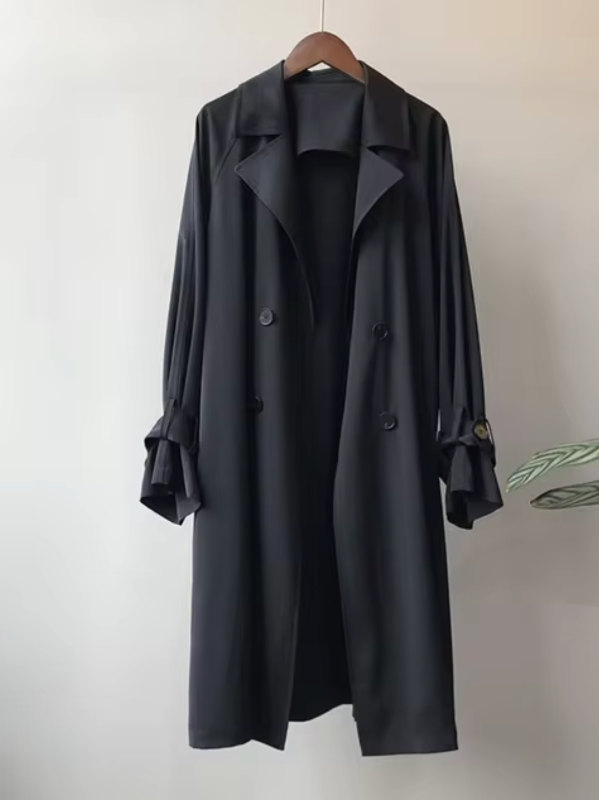 Black Double-Breasted Longline Trench Coat displayed on a hanger, featuring notch lapels, button front, long sleeves, and button-tab cuffs.