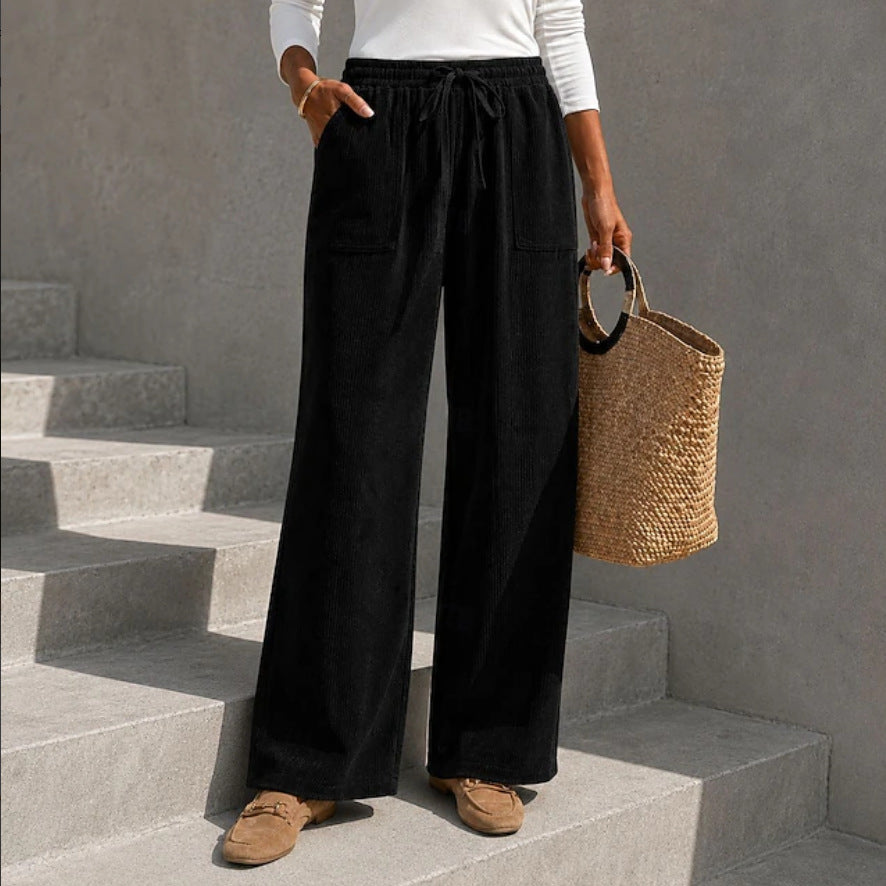 Black wide-leg corduroy pants featuring an elastic drawstring waistband and front patch pockets on concrete stairs.