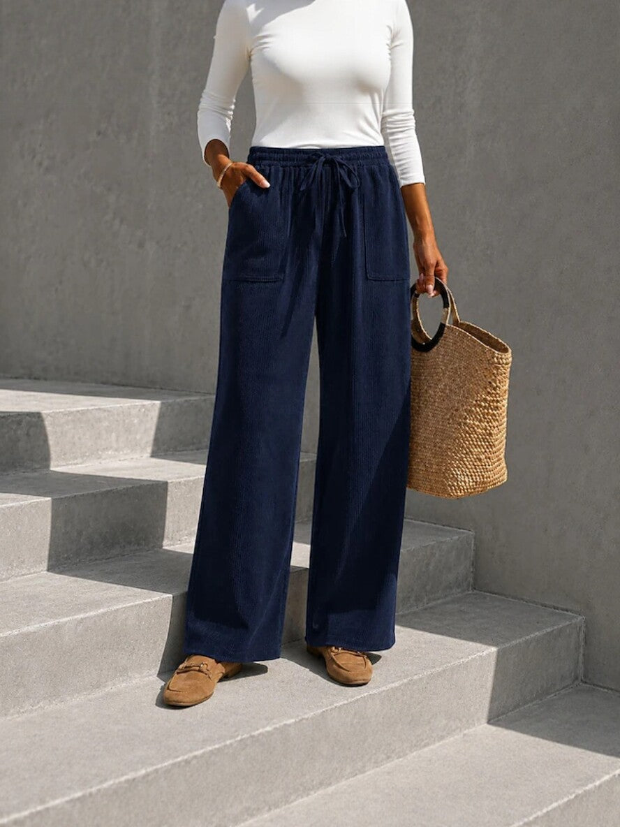 Navy blue wide-leg corduroy pants with an elastic drawstring waist and front patch pockets, styled with a white long-sleeve top.