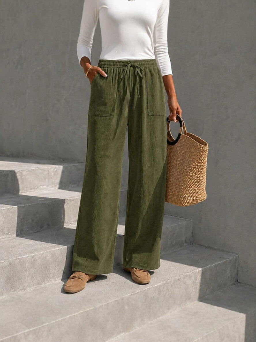 Olive green wide-leg corduroy pants featuring an elastic drawstring waist and front patch pockets on concrete steps.