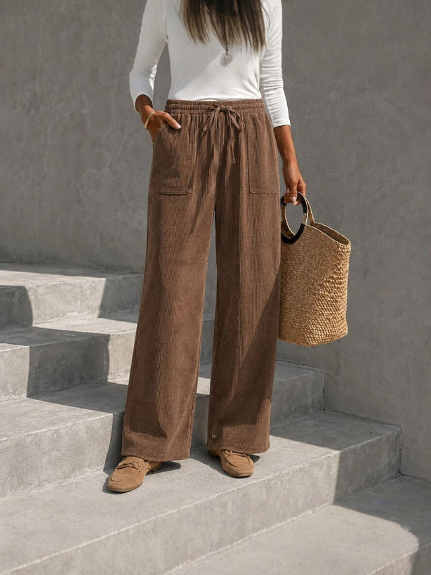 Brown wide-leg corduroy pants with an elastic drawstring waist and front patch pockets, styled with loafers.