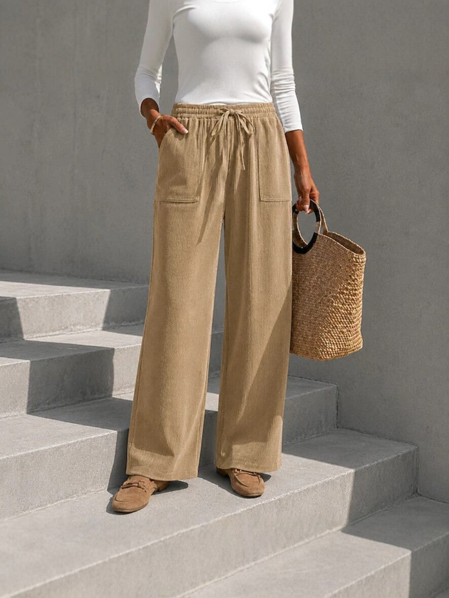 Beige wide-leg corduroy pants with an elastic drawstring waist and front patch pockets, styled with loafers on concrete steps.