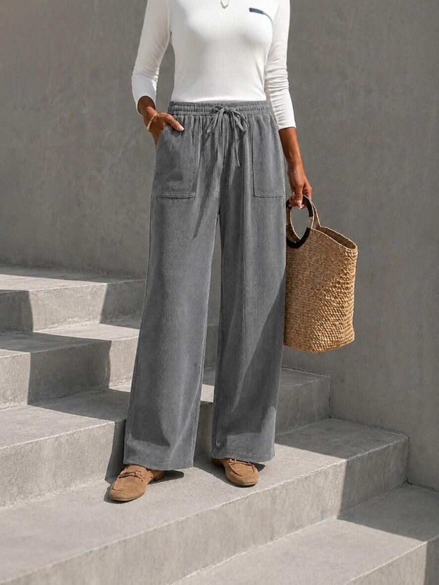 Gray wide-leg corduroy pants featuring an elastic drawstring waist and front patch pockets, styled with loafers on concrete steps.