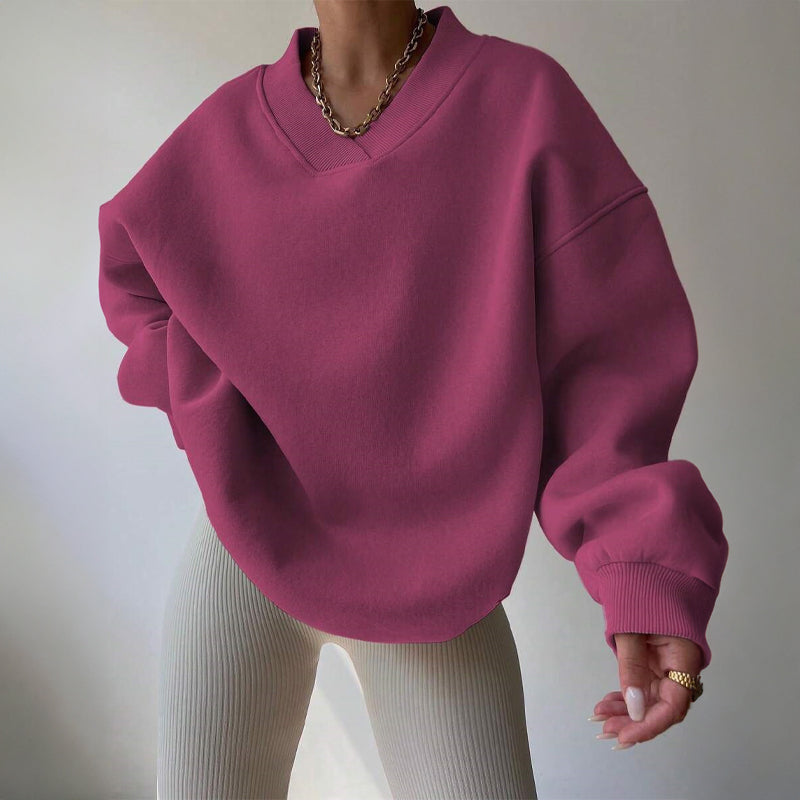 Pink oversized V-neck sweatshirt with dropped shoulders, ribbed cuffs, and a relaxed fit, styled with light-colored pants.
