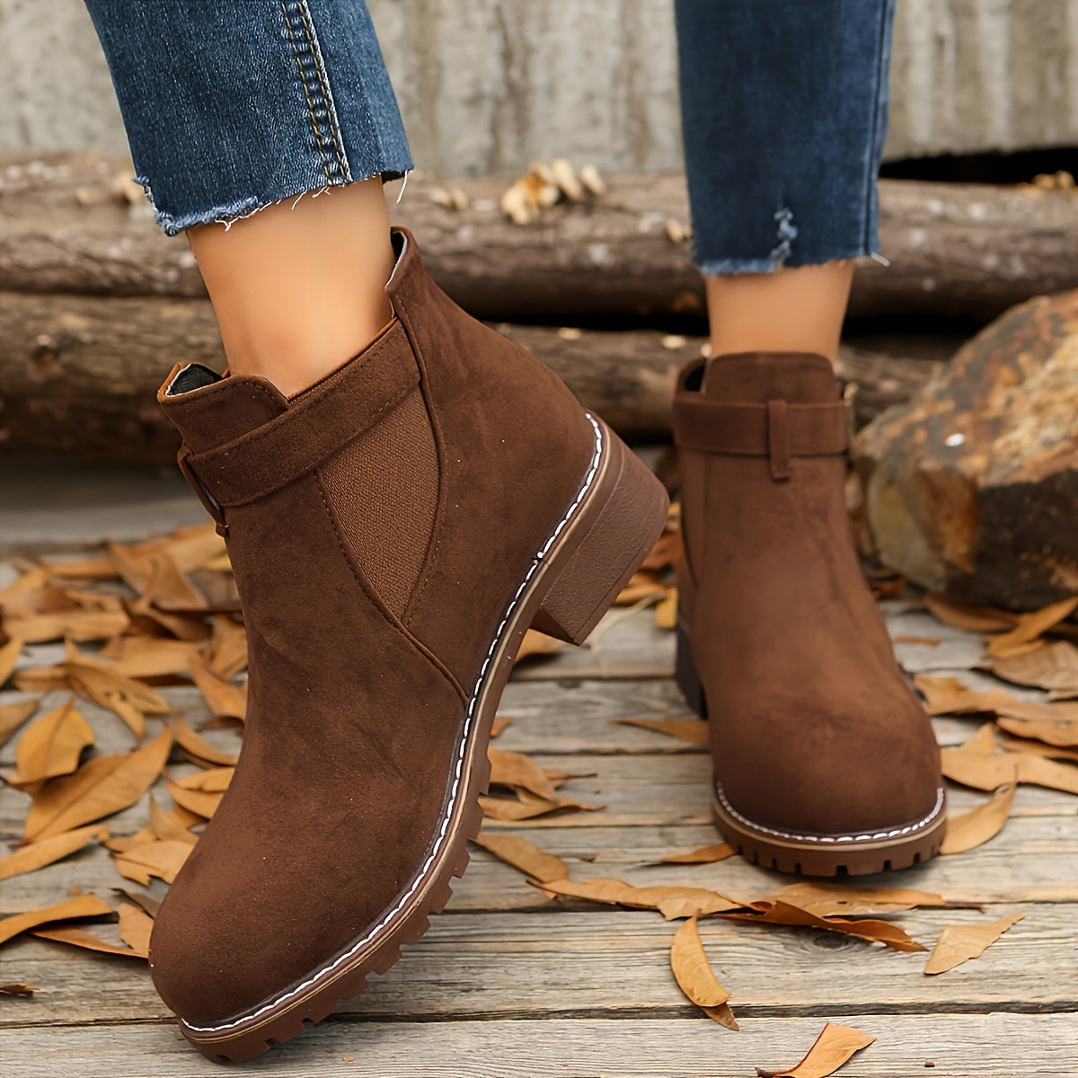 Brown suede Chelsea boots with buckle straps, elastic side panels, and rugged lug soles worn with blue denim jeans.