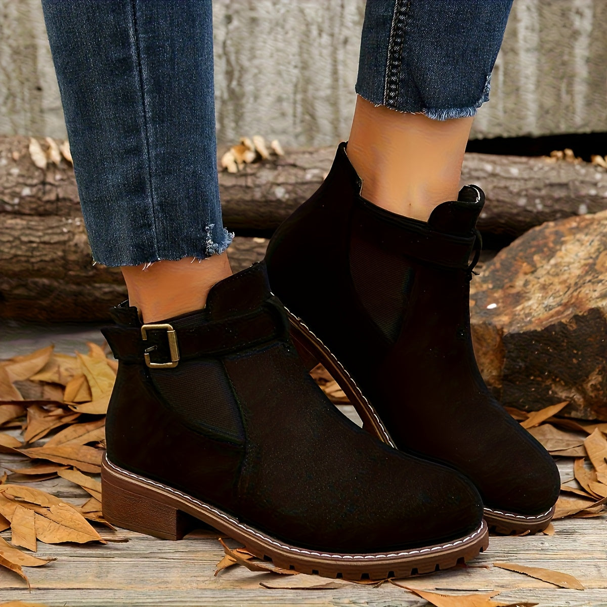 Black suede Chelsea boots featuring a buckle strap, elastic side panels, and a rugged lug sole with a low block heel.