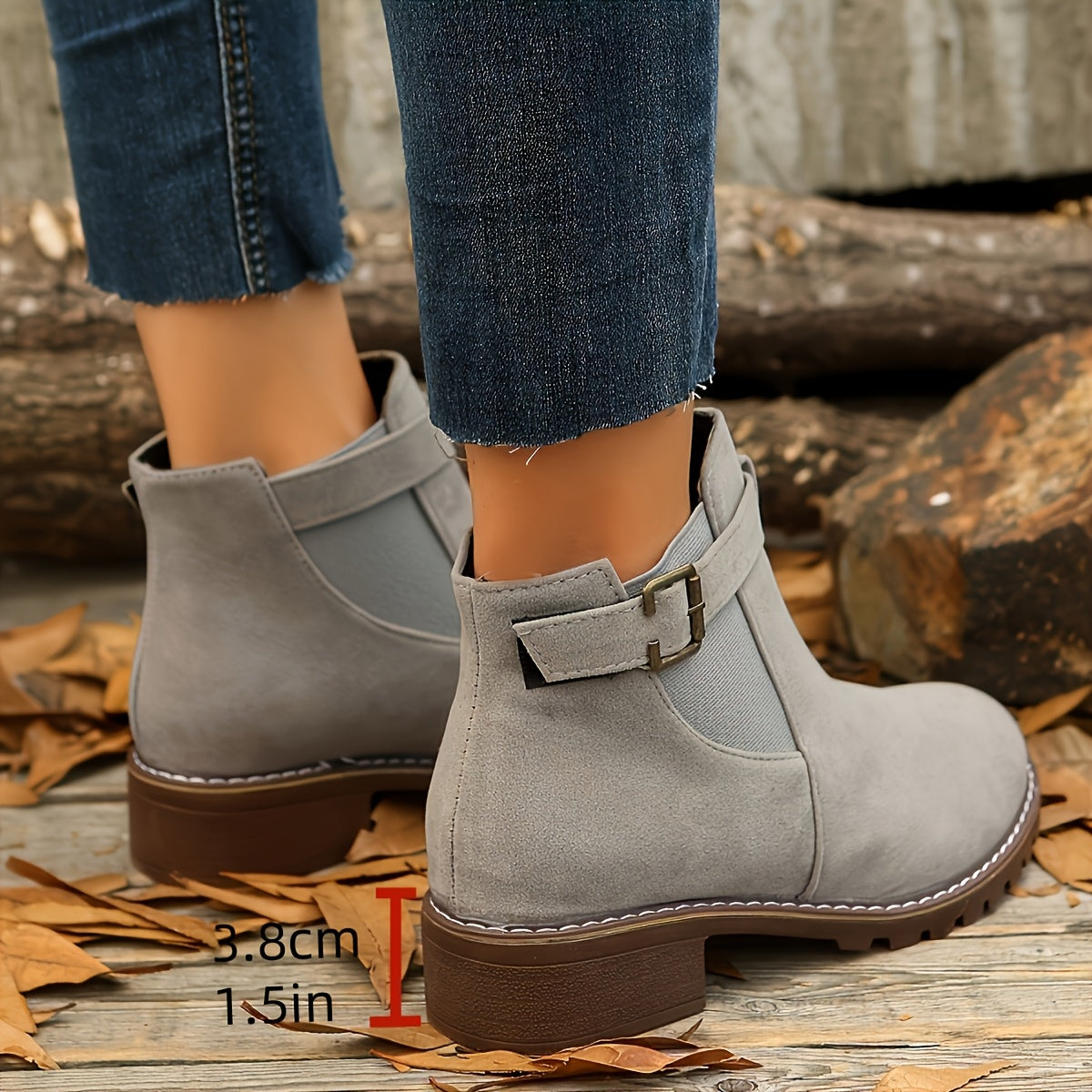 Grey suede Chelsea boots with a buckle strap, elastic side panels, and a 1.5-inch lug sole block heel on a wooden surface.