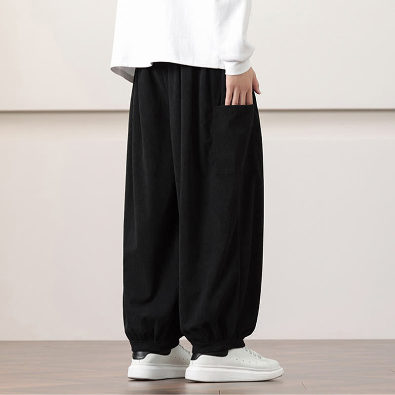 Black fine-wale corduroy harem pants with side patch pockets and cuffed ankles, styled with a white tee and sneakers.