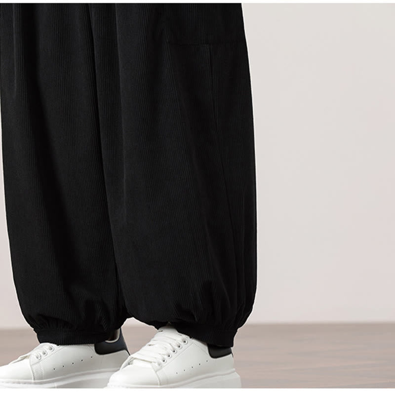Black fine-wale corduroy harem pants with side patch pockets and gathered elastic cuffs worn with white sneakers.