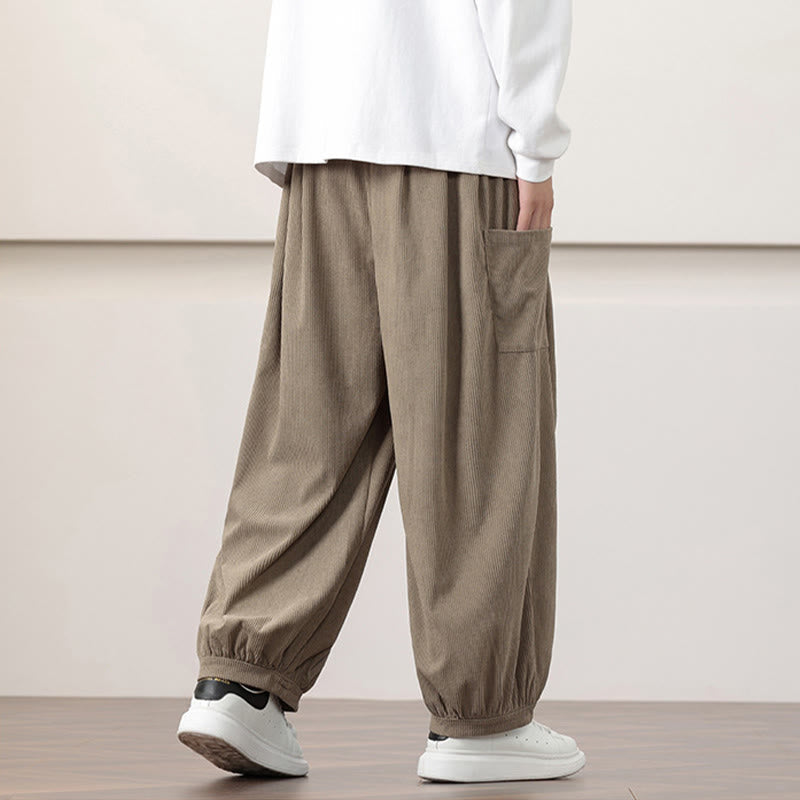 Dark khaki fine-wale corduroy harem pants with side patch pockets, relaxed fit, and gathered elastic cuffs over white sneakers.