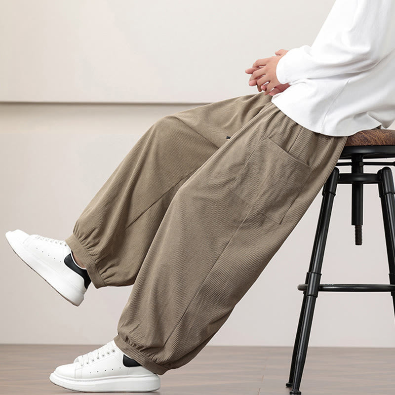 Dark khaki fine-wale corduroy harem pants with side patch pockets and cuffed ankles, styled with white sneakers.
