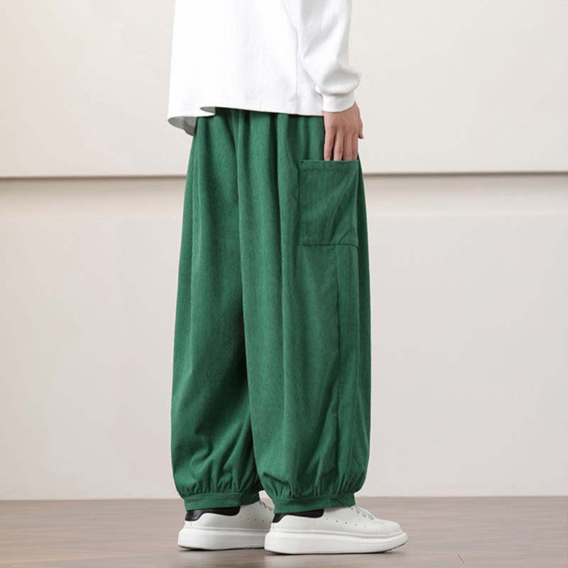 Green fine-wale corduroy harem pants with side patch pockets and cuffed ankles, styled with a white long-sleeve tee.