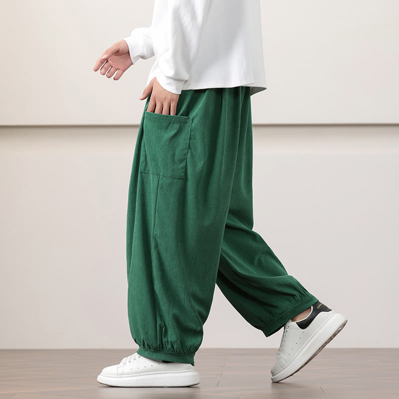 Dark green fine-wale corduroy harem pants featuring side patch pockets and cuffed ankles, styled with white sneakers.