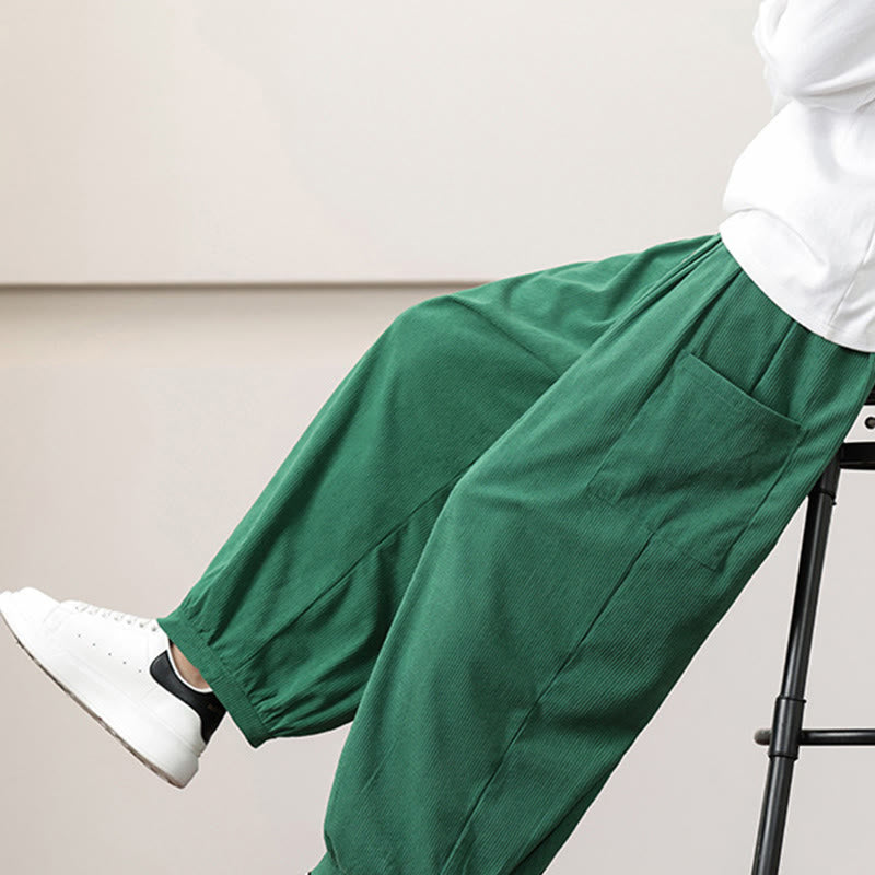 Green fine-wale corduroy harem pants with side patch pockets and cuffed ankles, styled with a white tee and sneakers.