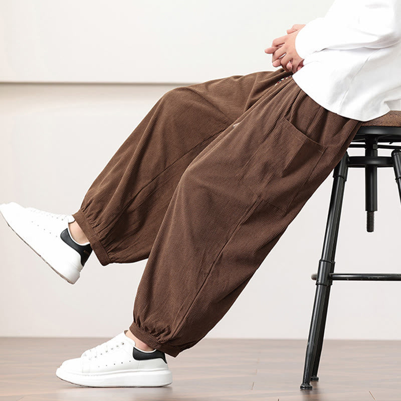 Brown fine-wale corduroy harem pants featuring side patch pockets, a drawstring waist, and cuffed ankles worn with sneakers.