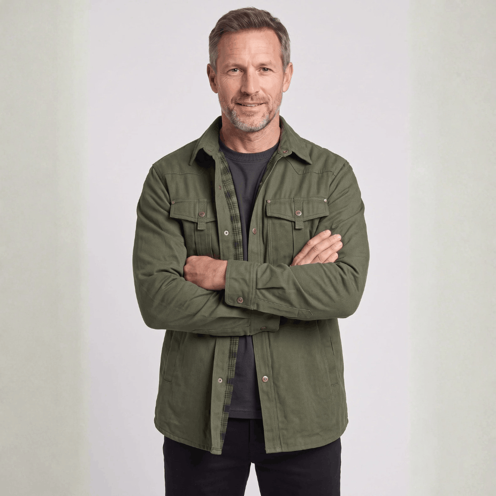 Front view of a model with arms crossed wearing an olive green canvas barn jacket with chest flap pockets.