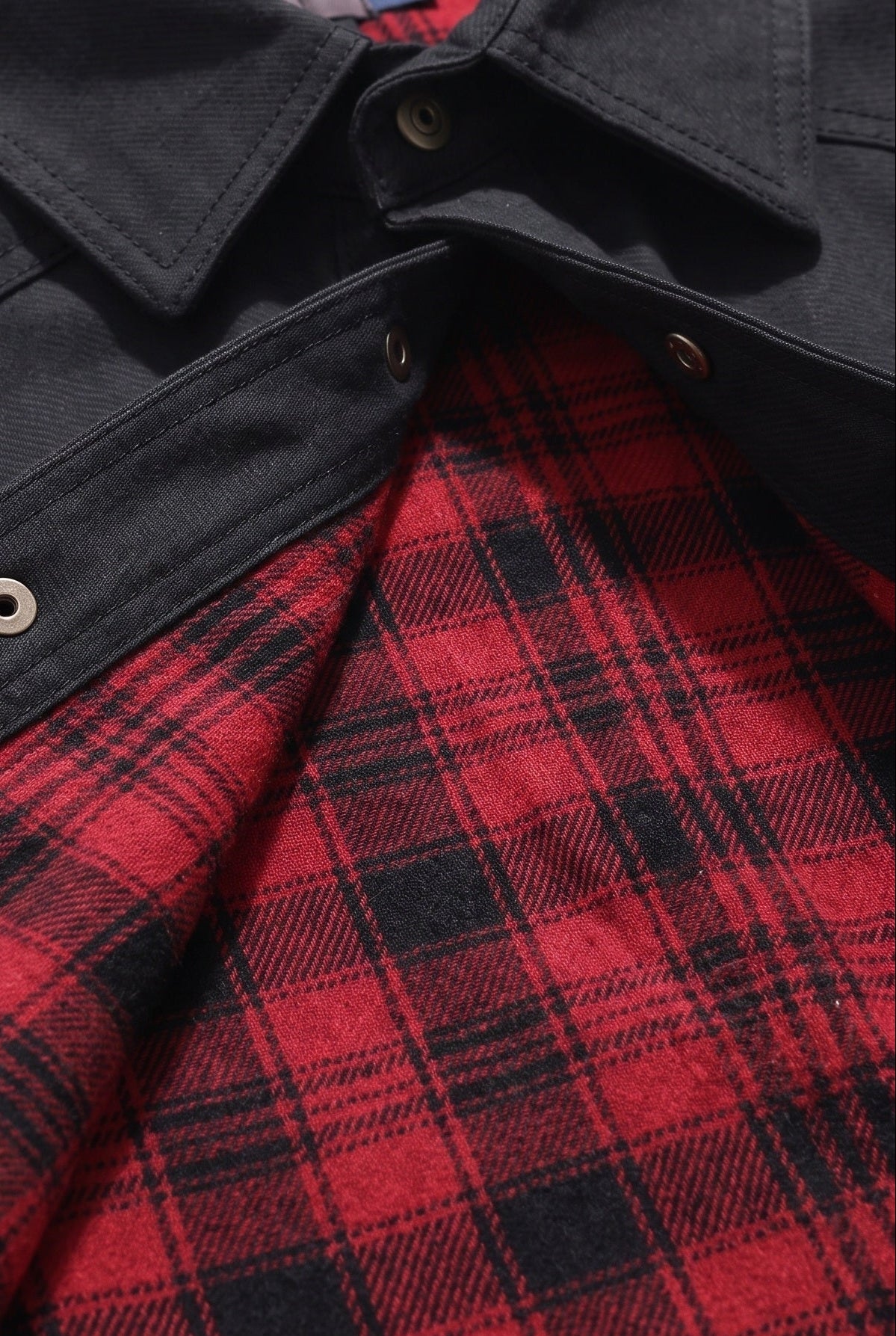Close-up view of the interior red and black buffalo plaid flannel lining and metal snap buttons of the jacket.
