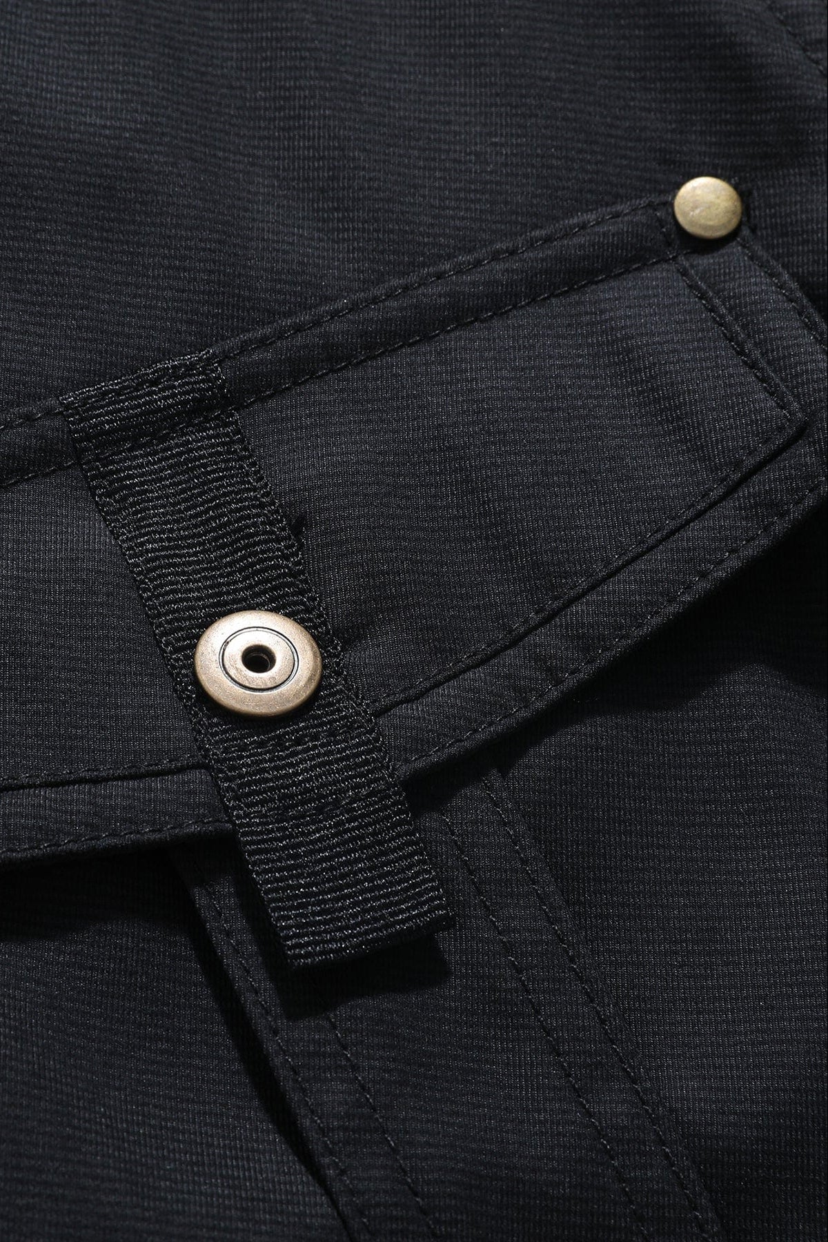 Macro detail view of a chest flap pocket with a metallic brass snap button closure on black canvas fabric.