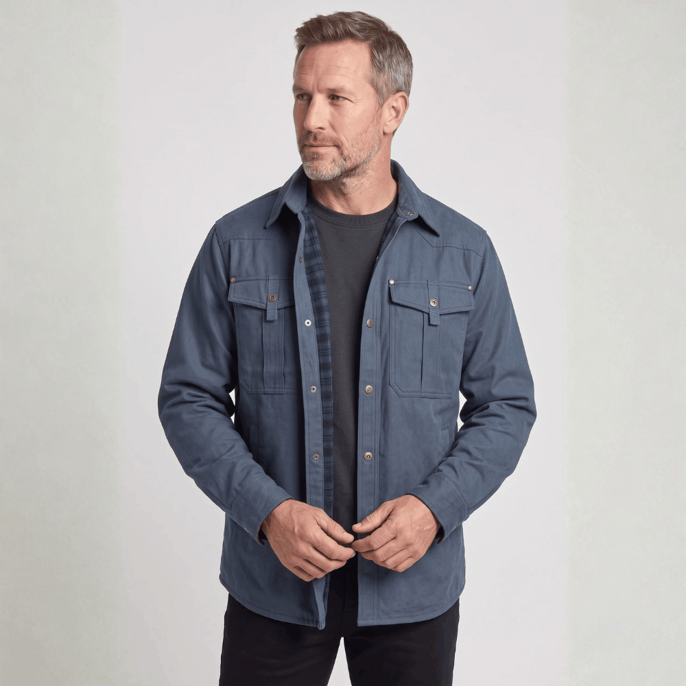 Front view of a model wearing a slate blue canvas barn jacket with metal snap closures over a dark t-shirt.