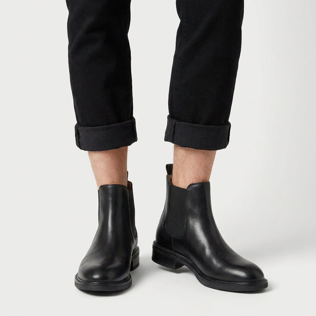 Black vegan leather Chelsea boots featuring a smooth polished finish, elastic side panels, and a low stacked heel.