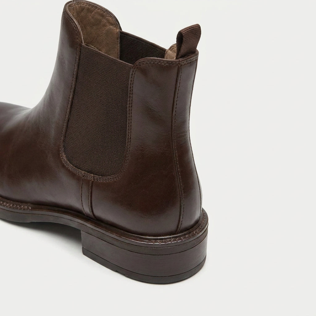 Dark brown vegan leather Chelsea boots featuring elastic side panels, a rear pull tab, and a low stacked heel.