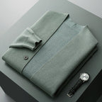 Sage green wool-blend V-neck cardigan with a structured knit, button-front detail, and folded sleeves on a grey surface.