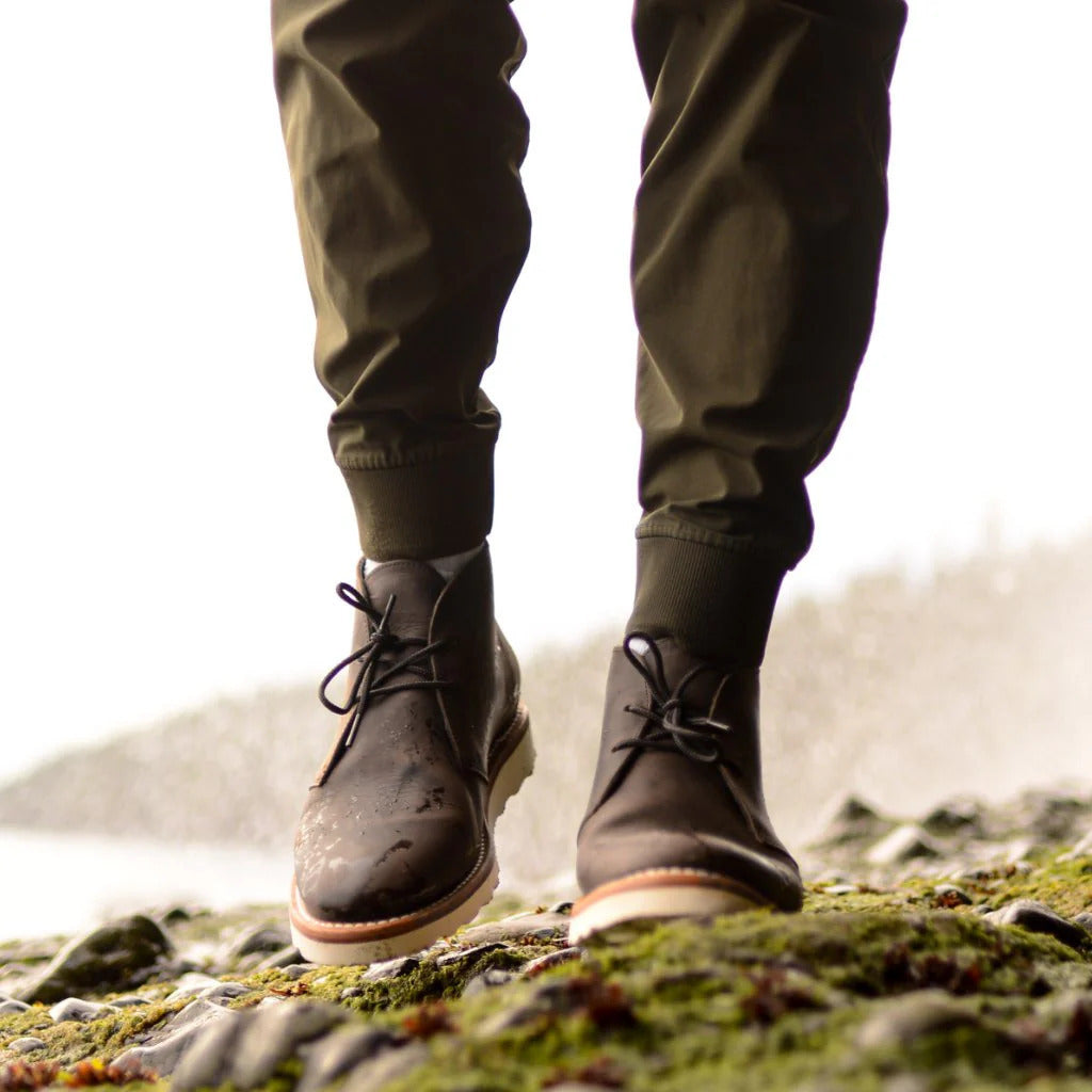 Dark brown napped leather chukka boots with two-eyelet lacing and a white treaded outsole, worn with olive green joggers.