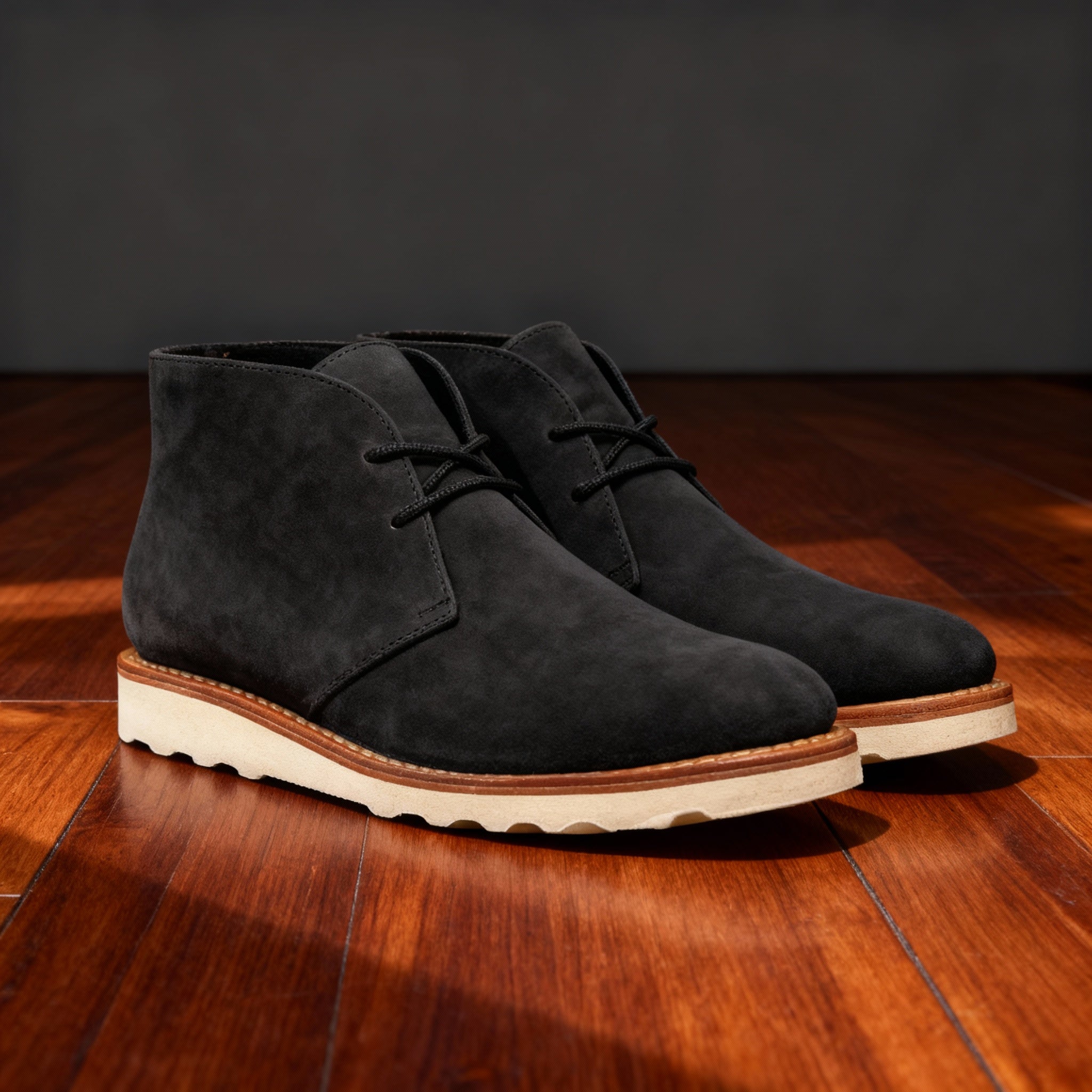 Black napped suede chukka boots featuring a two-eyelet lace-up front, rounded toe, and a thick, treaded white rubber sole.