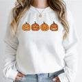 Close-up front view of a model wearing the white relaxed crewneck sweatshirt printed with four orange Halloween jack-o'-lantern pumpkin faces.
