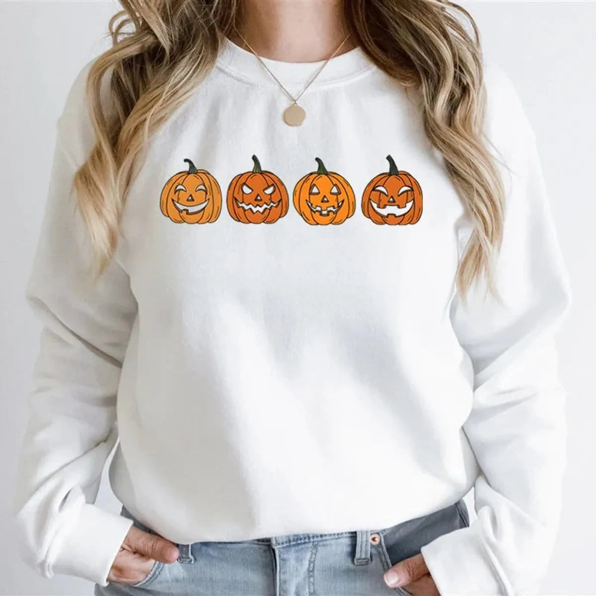 Close-up front view of a model wearing the white relaxed crewneck sweatshirt printed with four orange Halloween jack-o'-lantern pumpkin faces.
